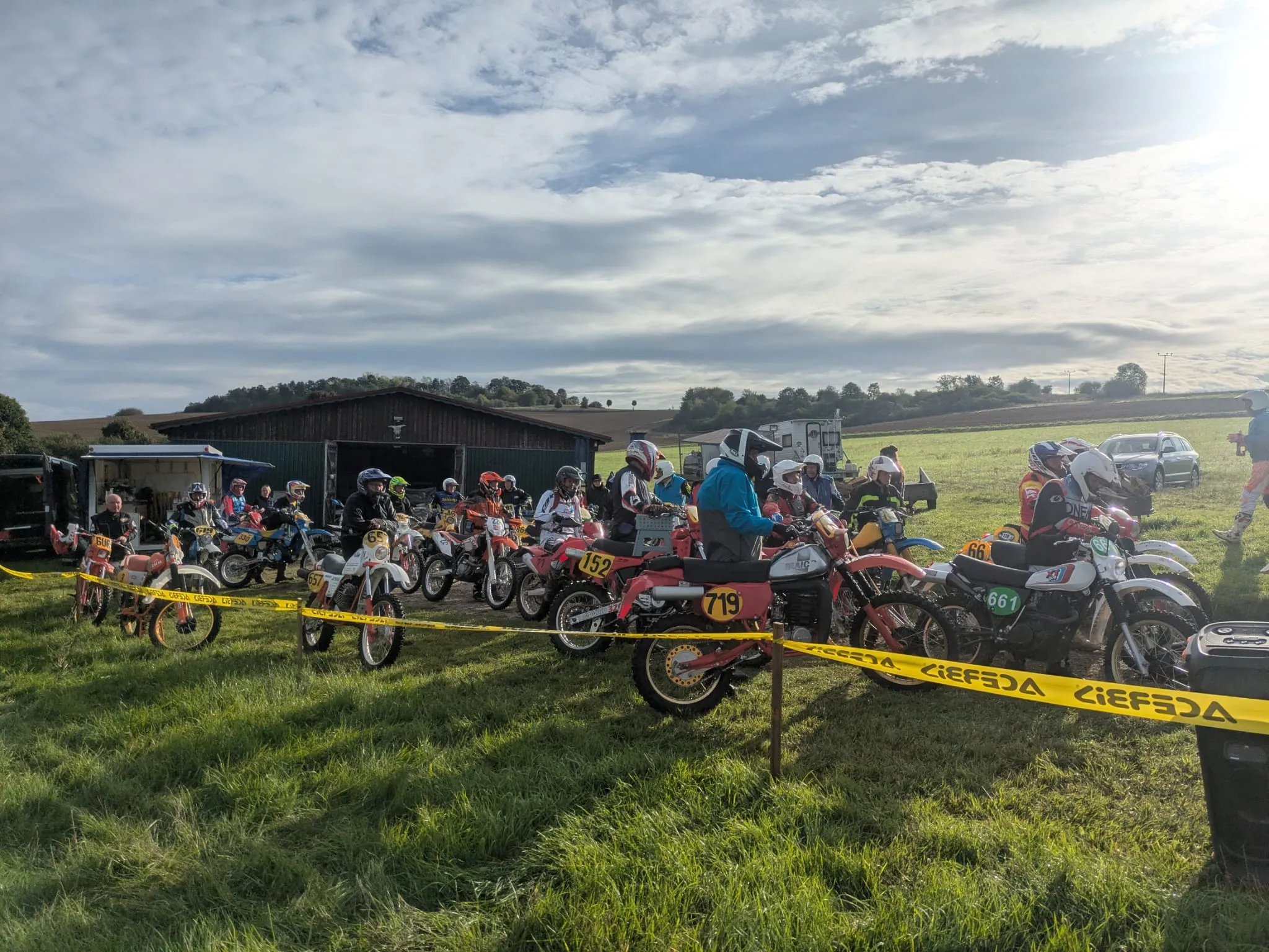 Fahrer mit klassischen Enduro-Motorrädern auf einer Wiese vor dem Start