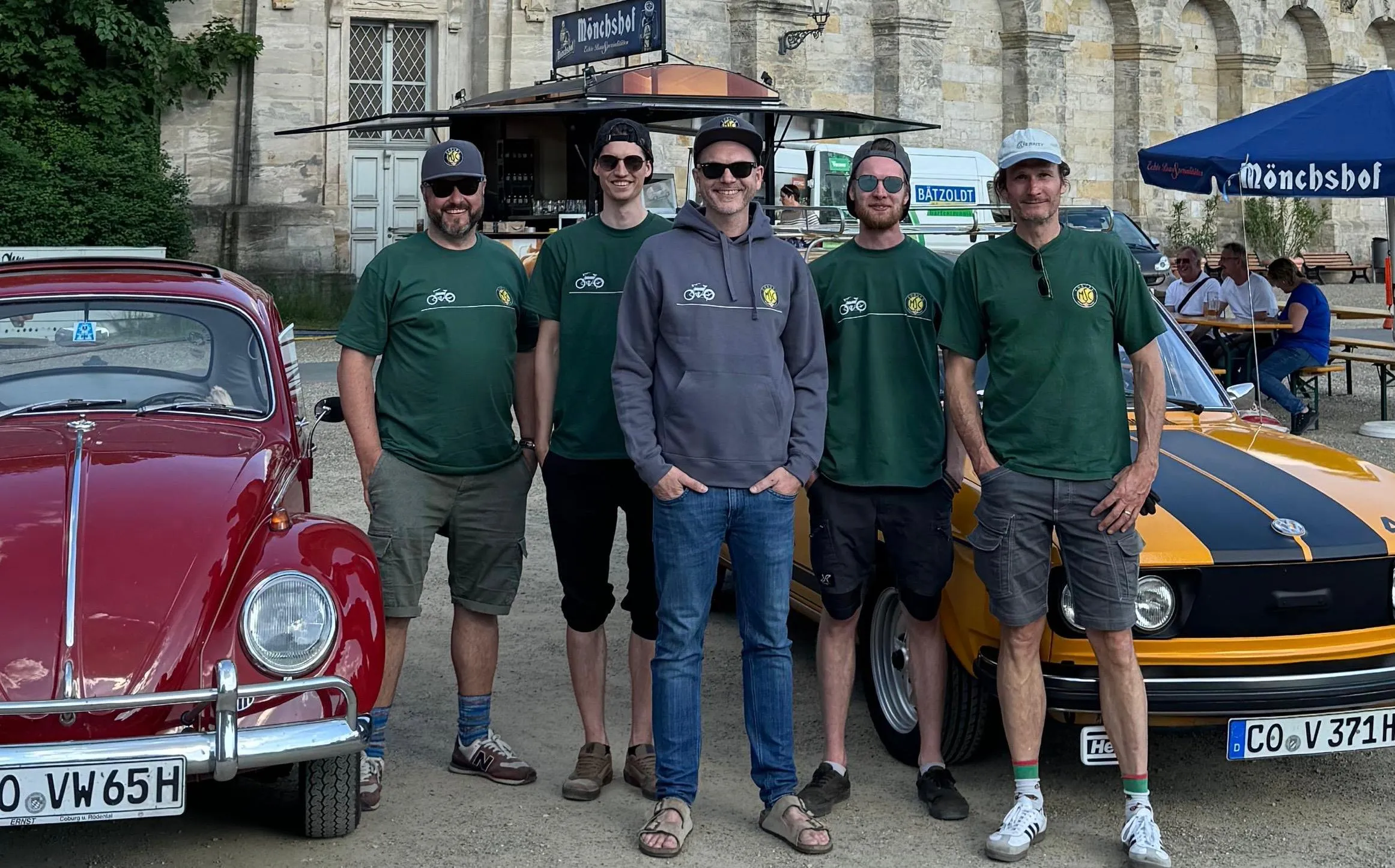 Fünf MSC-Mitglieder zwischen einem roten VW Käfer und einem gelben Oldtimer